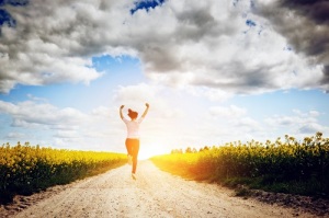 Happy young woman running and jumping for joy towards sun